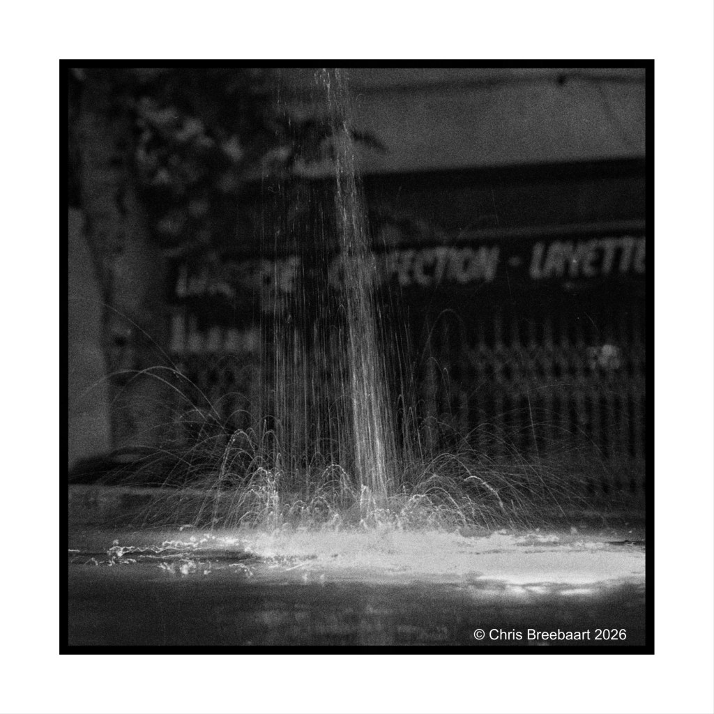 A black and white image of a fountain spraying water upwards against a blurred background.