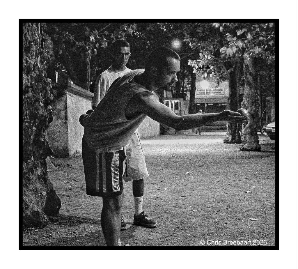 Two young men playing a game in a dimly lit park at night, one preparing to throw while the other watches.