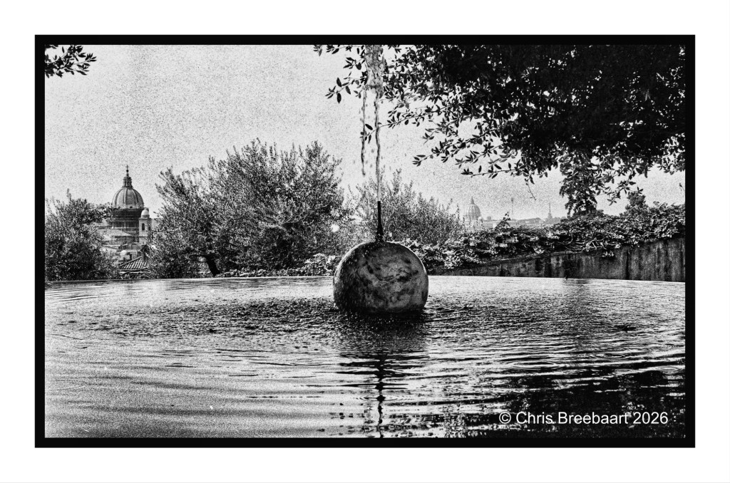 Black and white image of a round fountain sculpture in a rippling pool, surrounded by trees with a distant view of a dome structure.